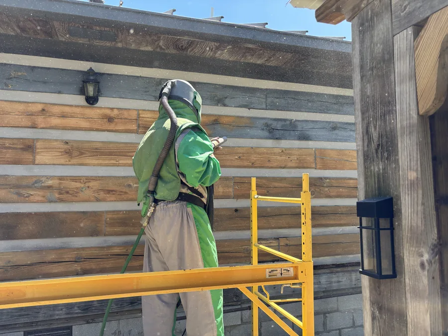 Technician media blasting the exterior wall of a log cabin from scaffolding